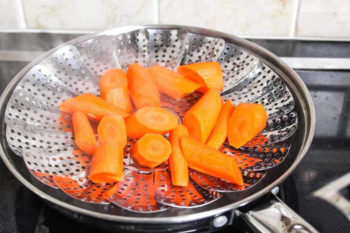 sliced carrots in a steamer basket on the stove