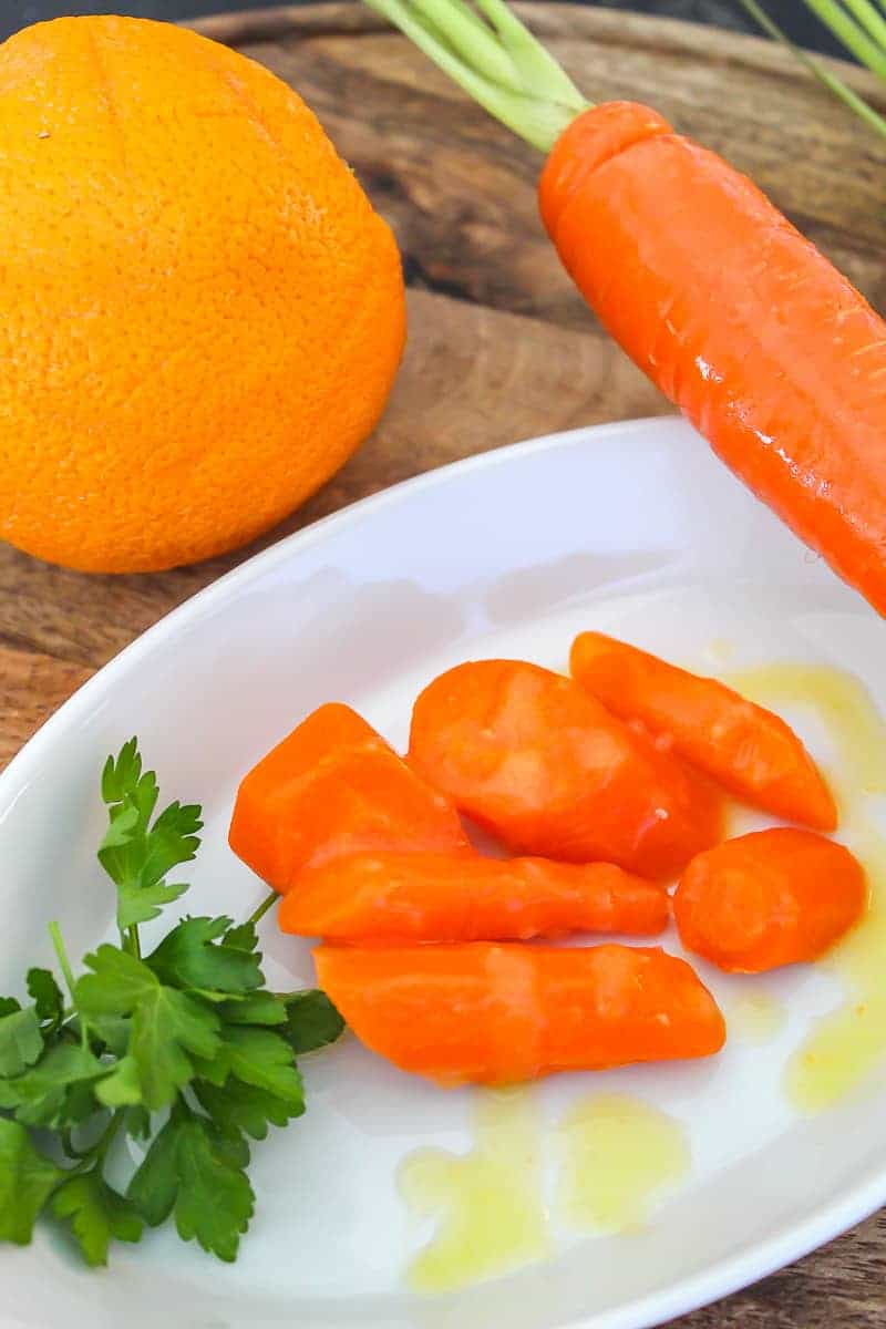 Orange glaze drizzled over sliced carrots in a white bowl