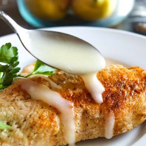 Lemon sauce being spooned and drizzled over chicken breast