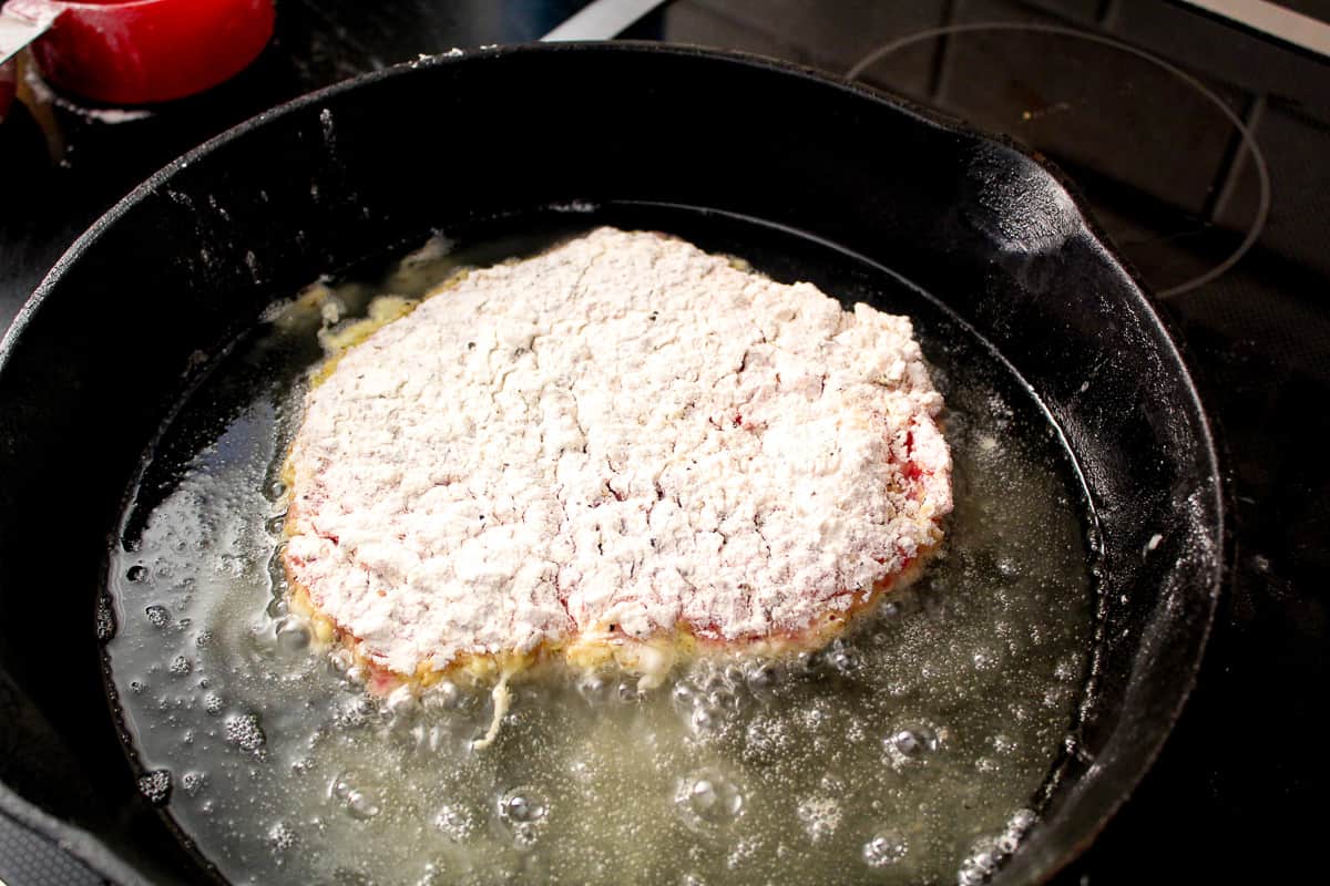 Chicken fried steak cooking in cast iron skillet