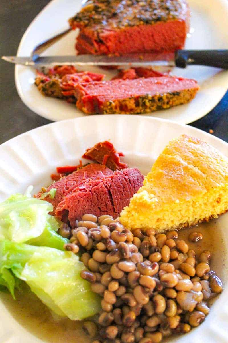 Peas, cabbage, corned beef and cornbread on white plate.