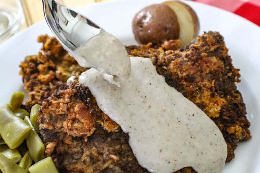 Cream gravy being spooned over chicken fried steak