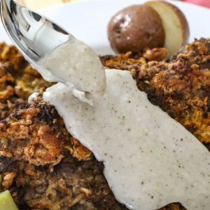 Cream gravy being spooned over chicken fried steak