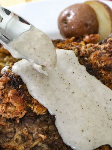 Cream gravy being spooned over chicken fried steak