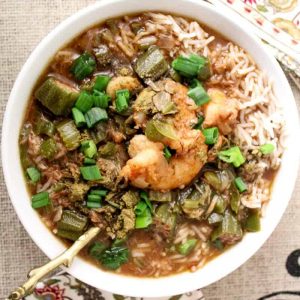 White bowl of gumbo with rice, green onions and seafood