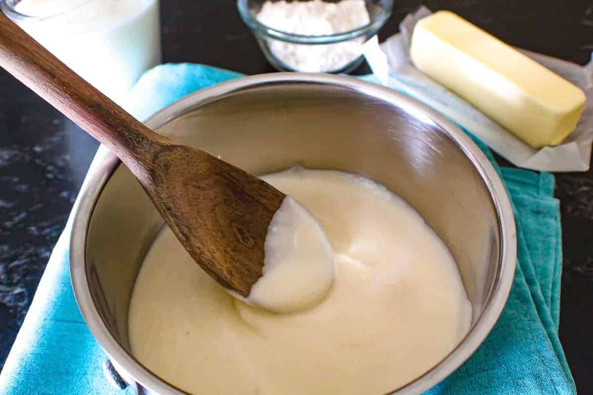 Cream sauce in pan with wooden spoon butter and flour in background