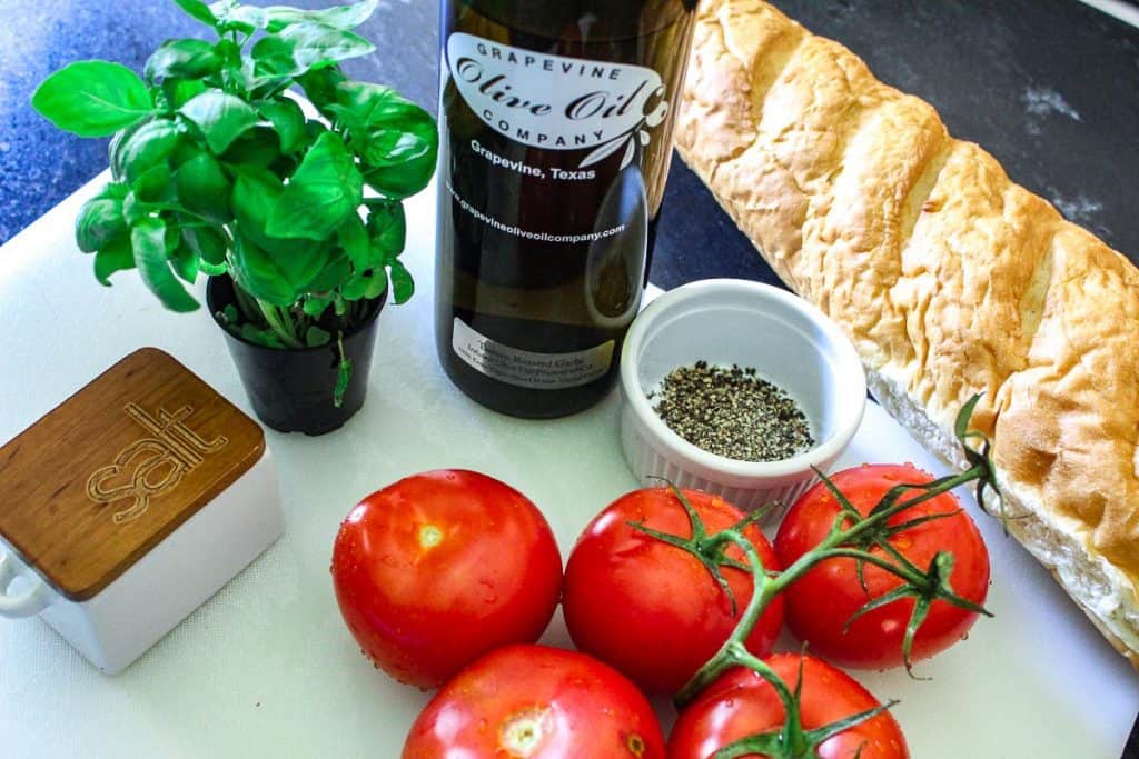 Tomatoes, basil, basil, salt, olive oil and bread on white cutting board