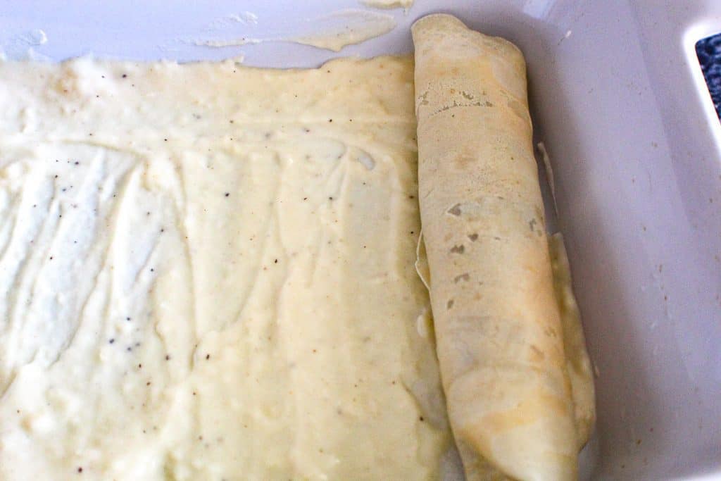 Crepe rolled with sausage in baking dish on top of sauce.