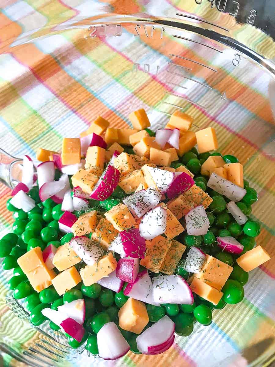 Clear bowl with red onion, cubed cheddar and green peas