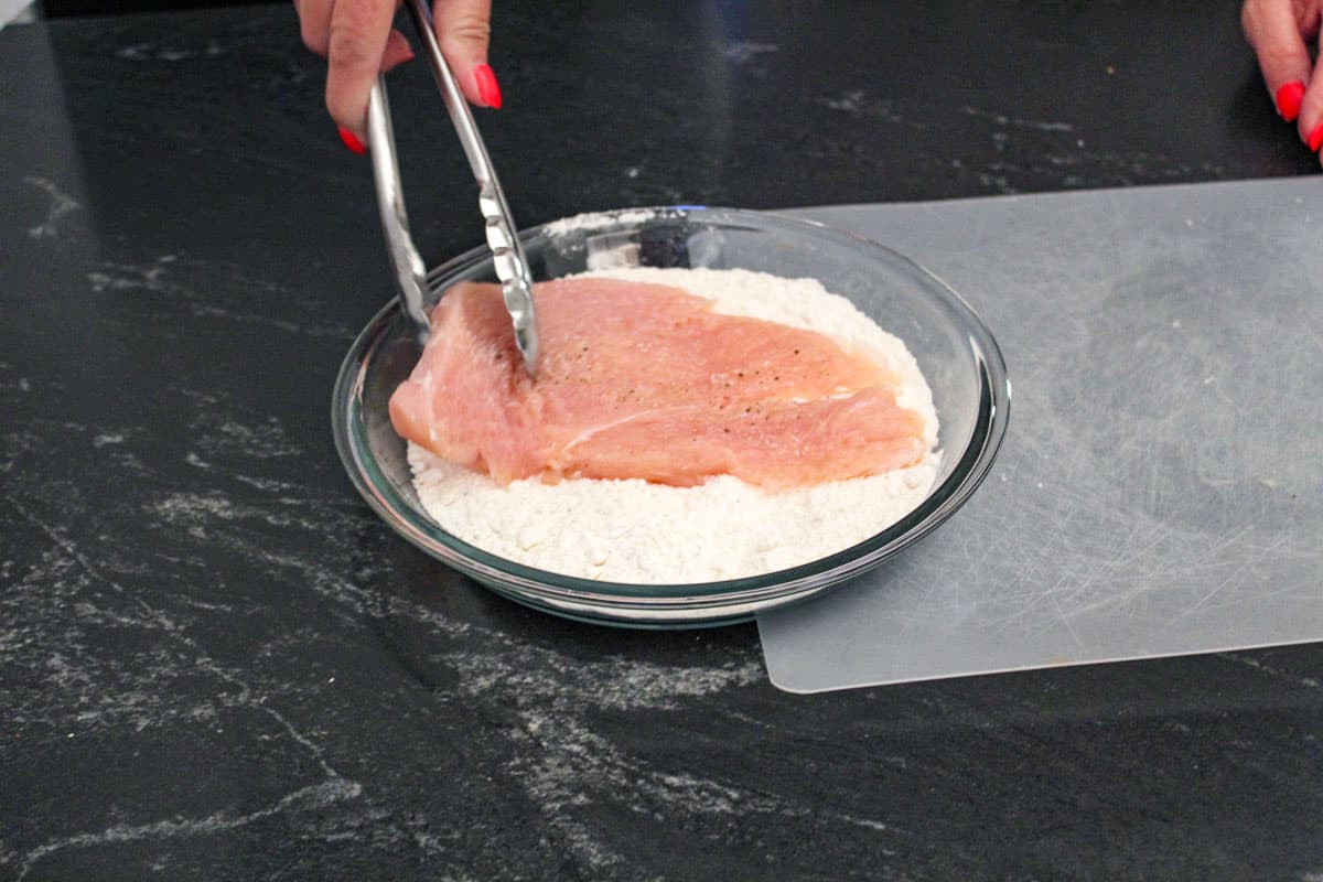 Chicken breast being dredged in flour