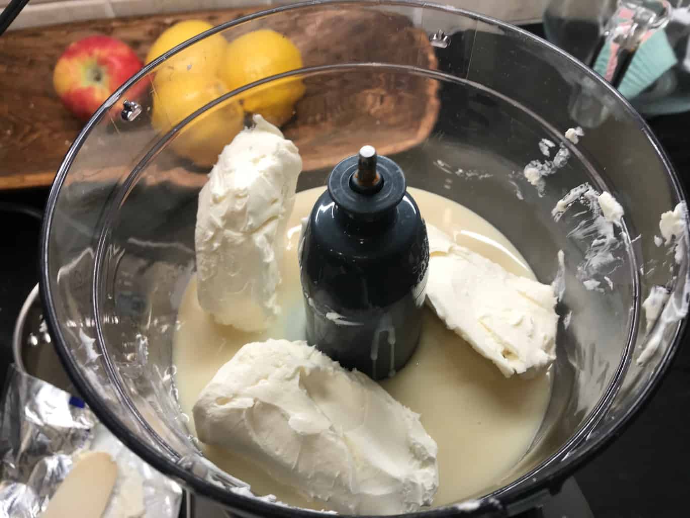 Food processor with condensed milk and cream cheese in it.