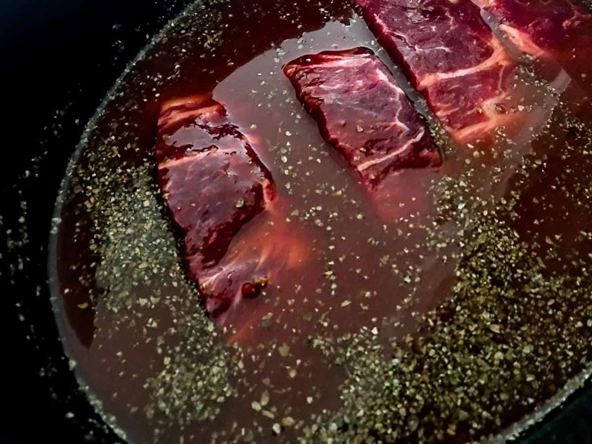 Country ribs in braising liquid in crockpot with marjoram sprinkled on top