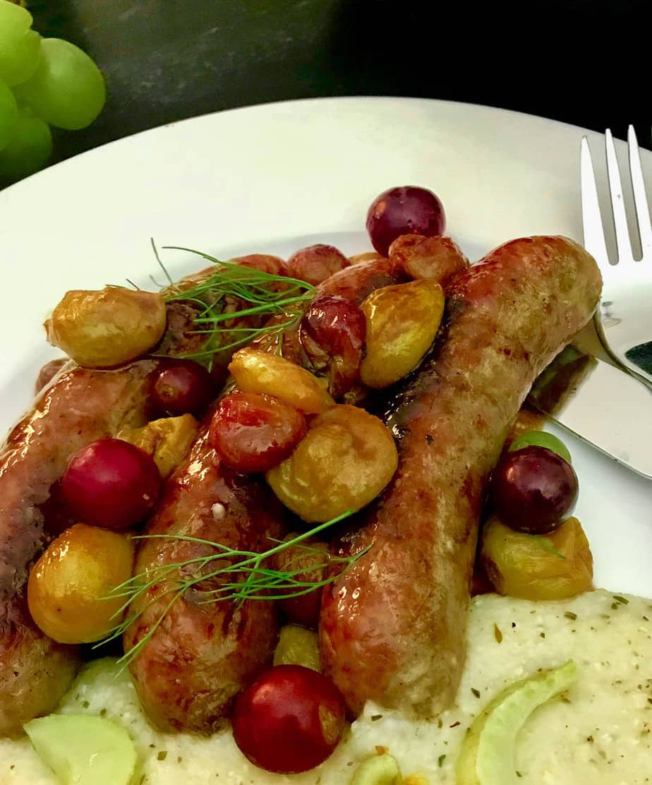 Italian sausage links and roasted grapes on white plate. 