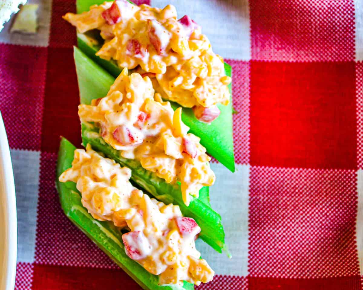 Three short celery stalks stuffed with pimento cheese on red checkered tablecloth