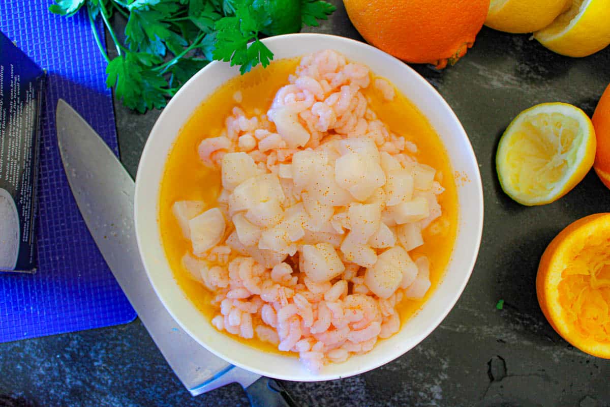 Shrimp and scallops marinating in white bowl of citrus juices