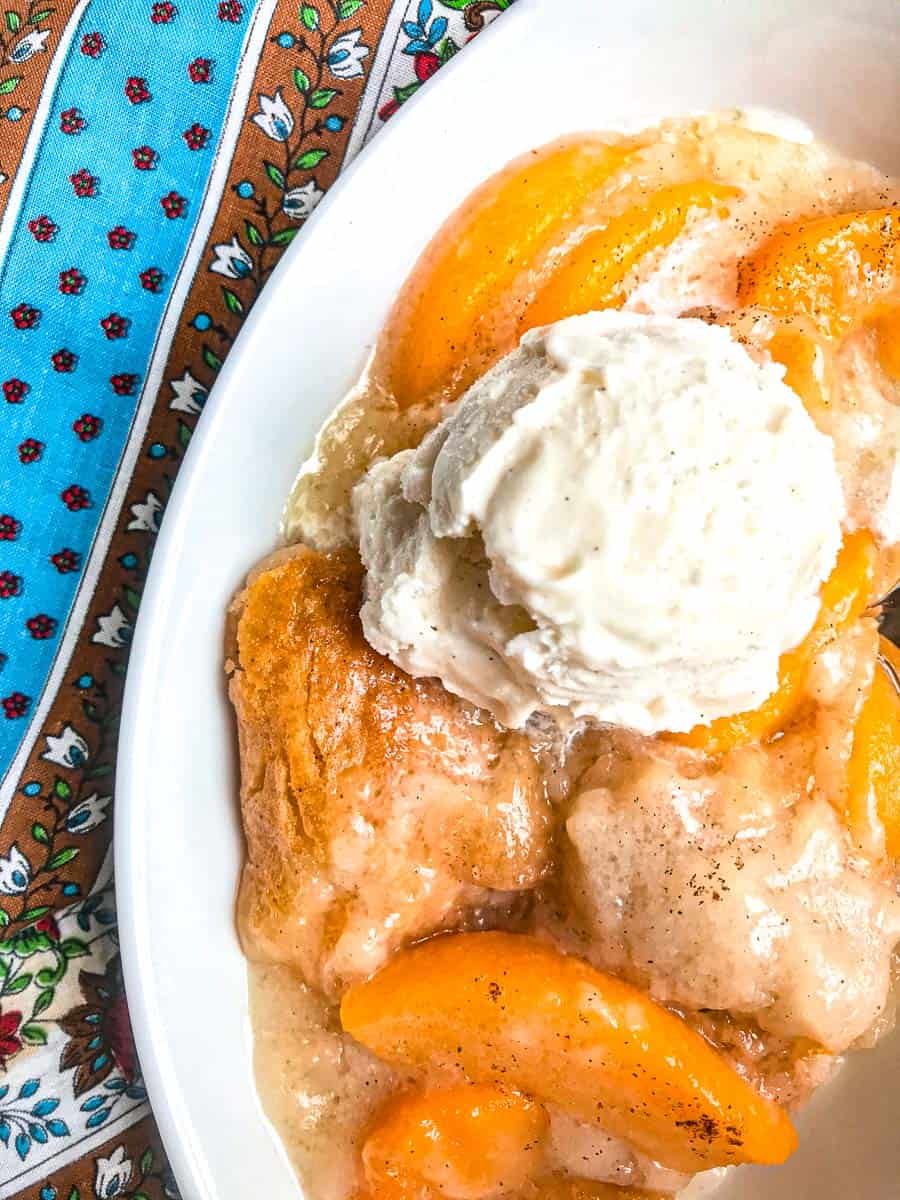 Peach cobbler topped with vanilla ice cream in white bowl