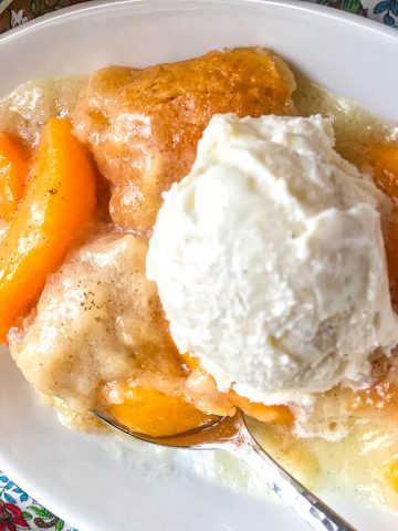 Peach Cobbler topped with vanilla ice cream in white oval dish