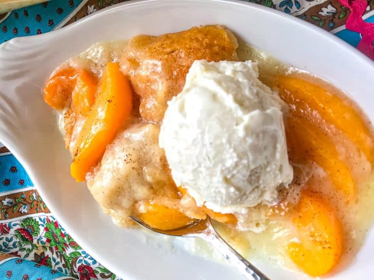 Peach Cobbler topped with vanilla ice cream in white oval dish