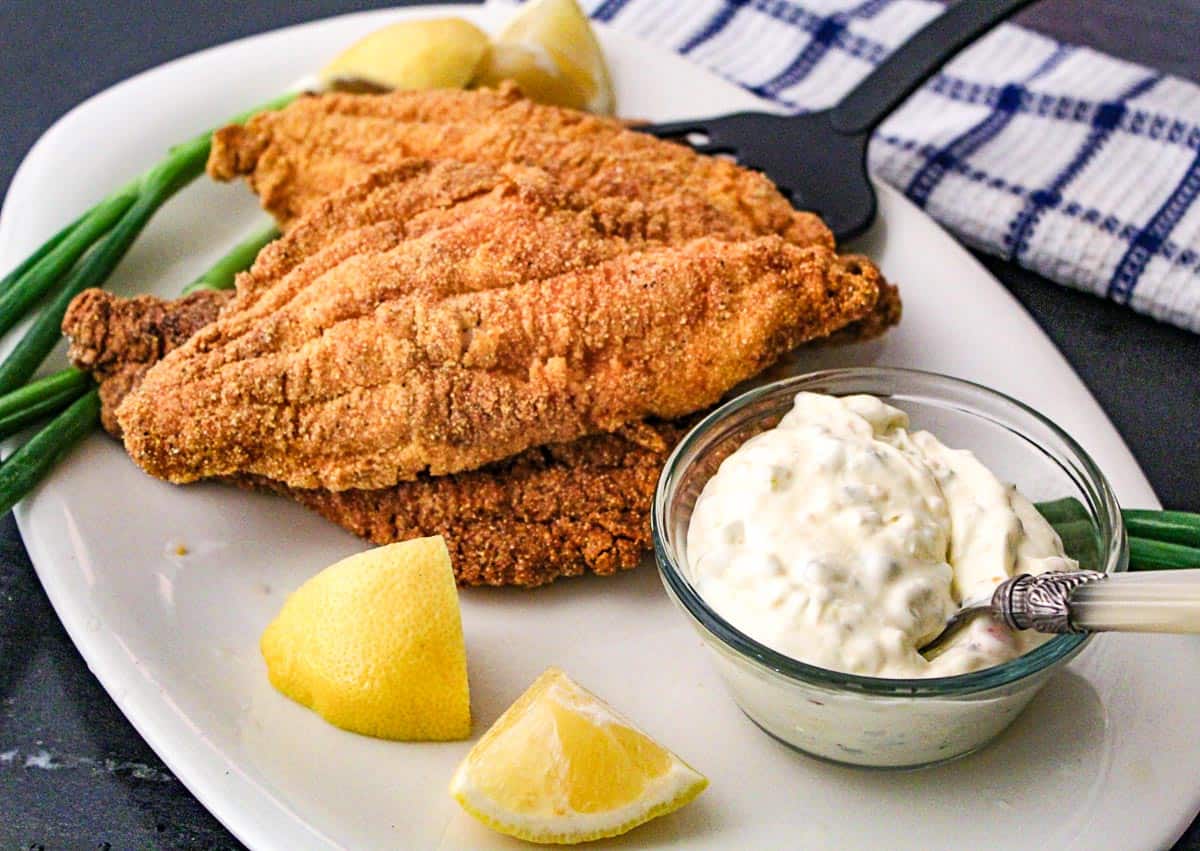 Fried catfish with lemon and tartar sauce on a white platte.