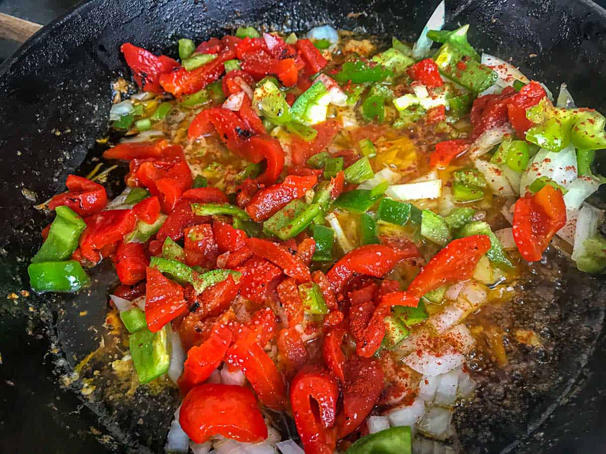 Onions, red peppers and green bell peppers in a cast iron skillet