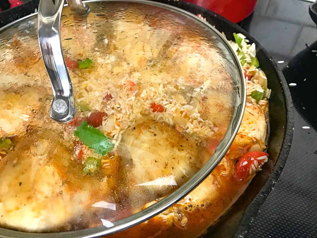 Clear lid being placed over skillet with chicken and veggies