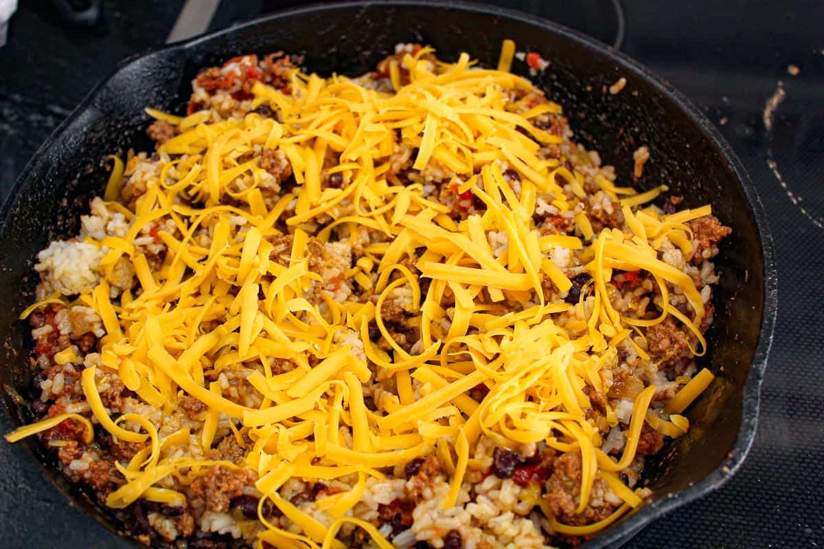 Shredded cheddar cheese over beef and rice in cast iron skillet