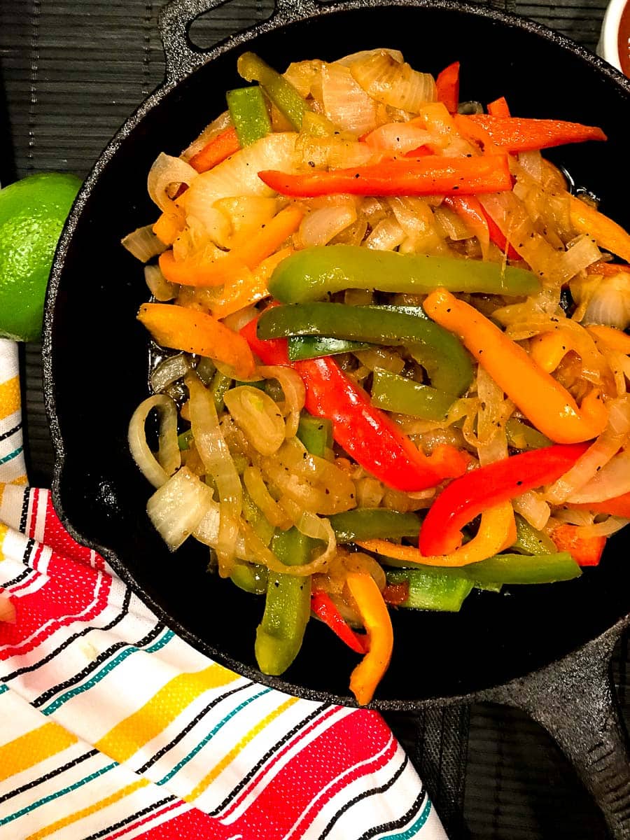Sliced red, yellow and green bell peppers and onions in cast iron skillet.
