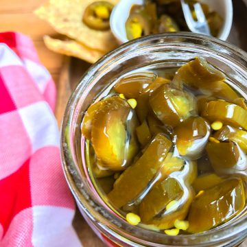 Candied jalapenos in a jar next to a red and white checkered napkin