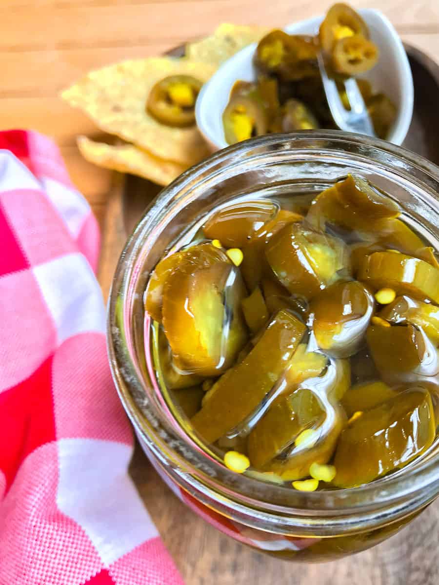 Candied jalapenos in a jar next to a red and white checkered napkin.