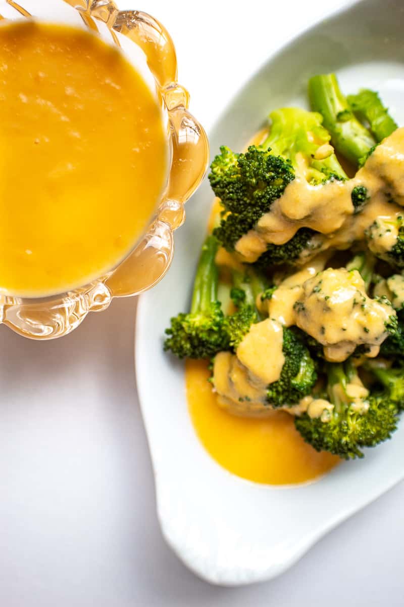 Broccoli florets with cheese sauce in white serving dish.