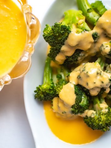 Cheese sauce drizzled over broccoli in white bowl with side of cheese sauce