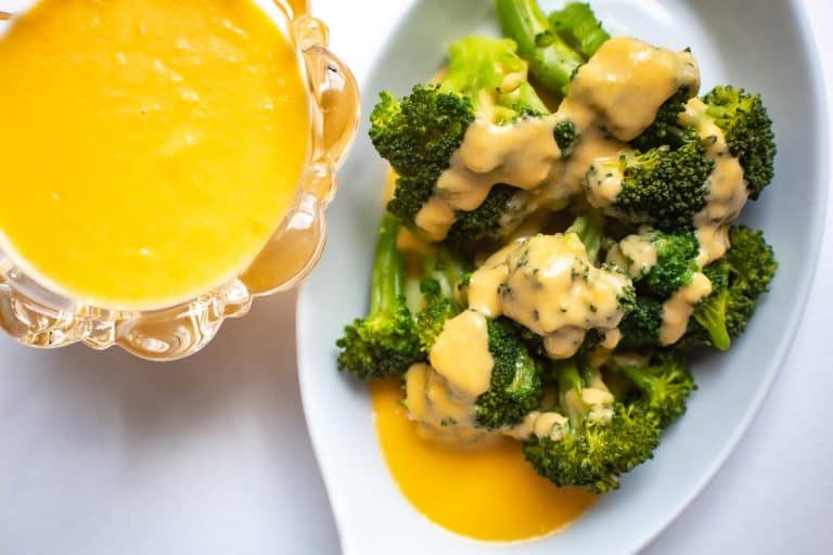 Cheese sauce drizzled over broccoli in white bowl with side of cheese sauce