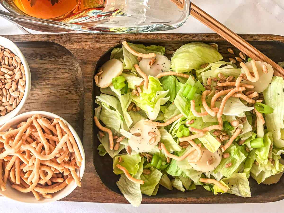 Salad on wooden plate with a side of noodles and sunflower seeds