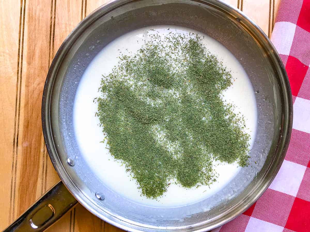 Dried herbs added to milk and roux mixture in saucepan