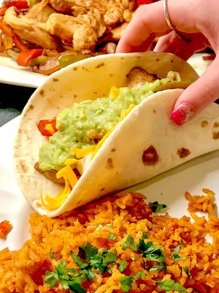 Someone holding a folded fajita with a side of rice on a white plate