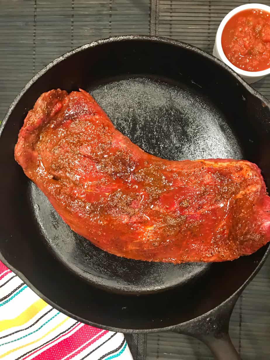 Seasoned and marinated flank steak in cast iron skillet.