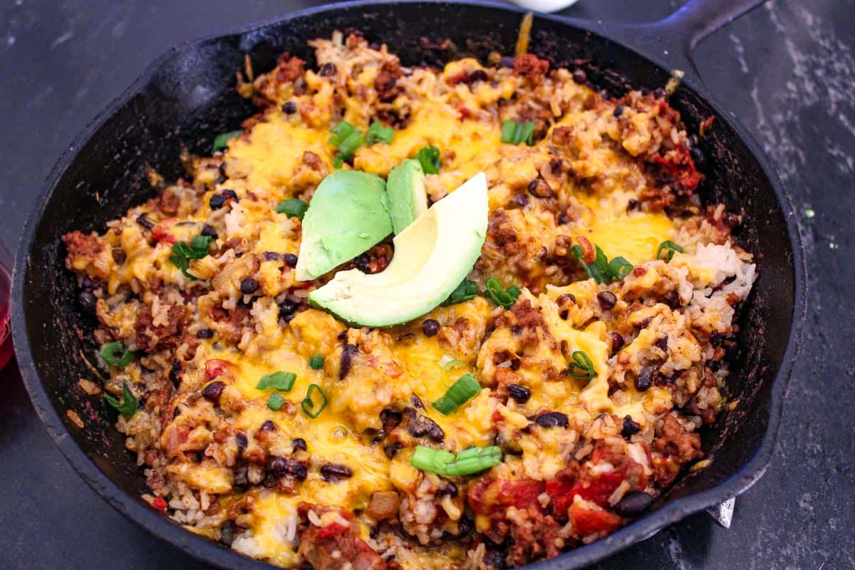 Mexican skillet supper in cast iron skillet garnished with green onion and avocado