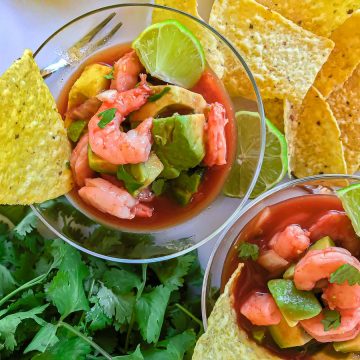 Shrimp and avocado in tomato broth garnished with lime wedge and tortilla chip