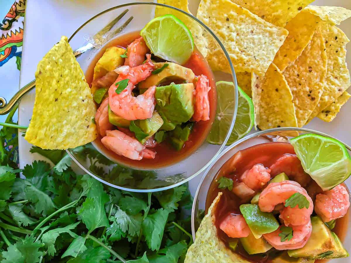 Shrimp and avocado in tomato broth garnished with lime wedge and tortilla chip
