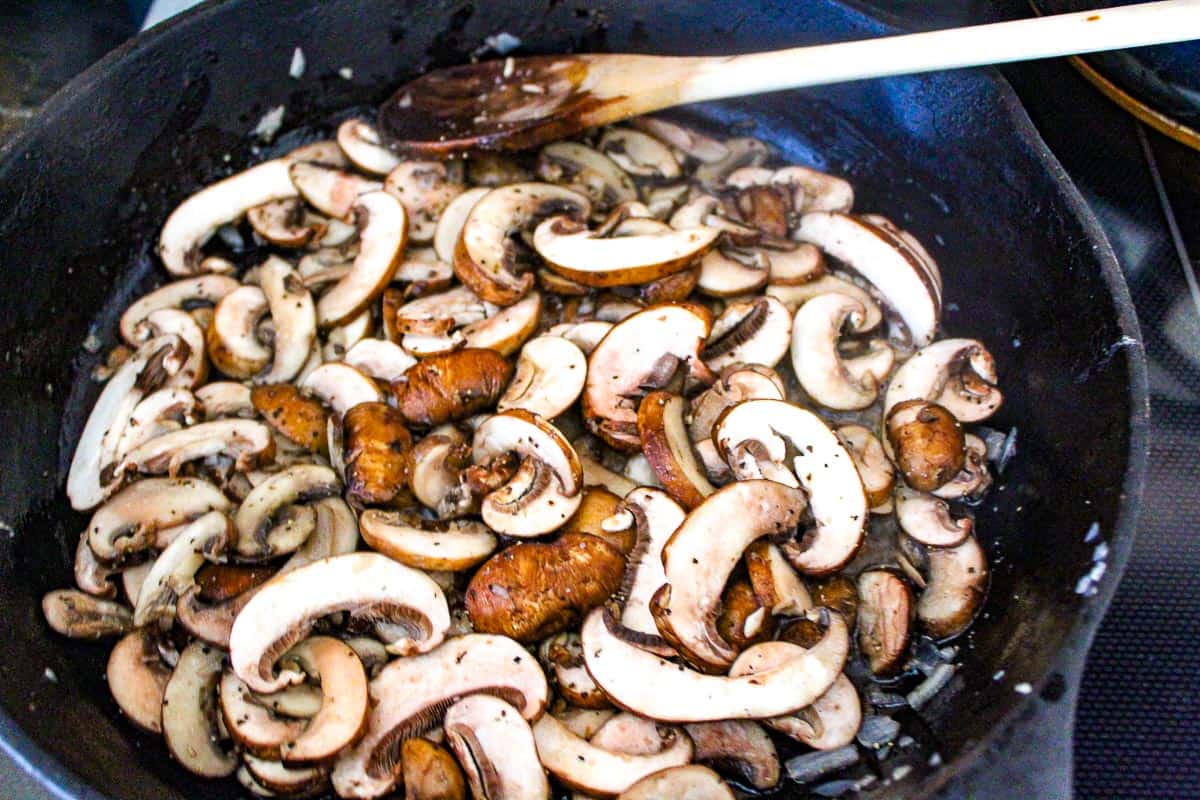 Sliced mushrooms sauteing in black skillet.