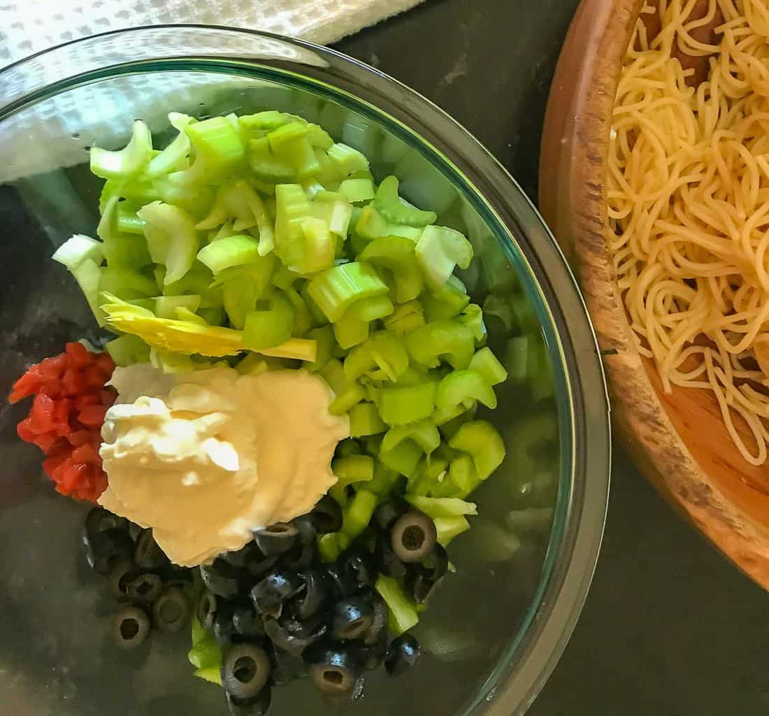 Ingredients in clear bowl next to cooked pasta