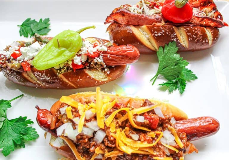Three hot dogs garnished differently on a white plate