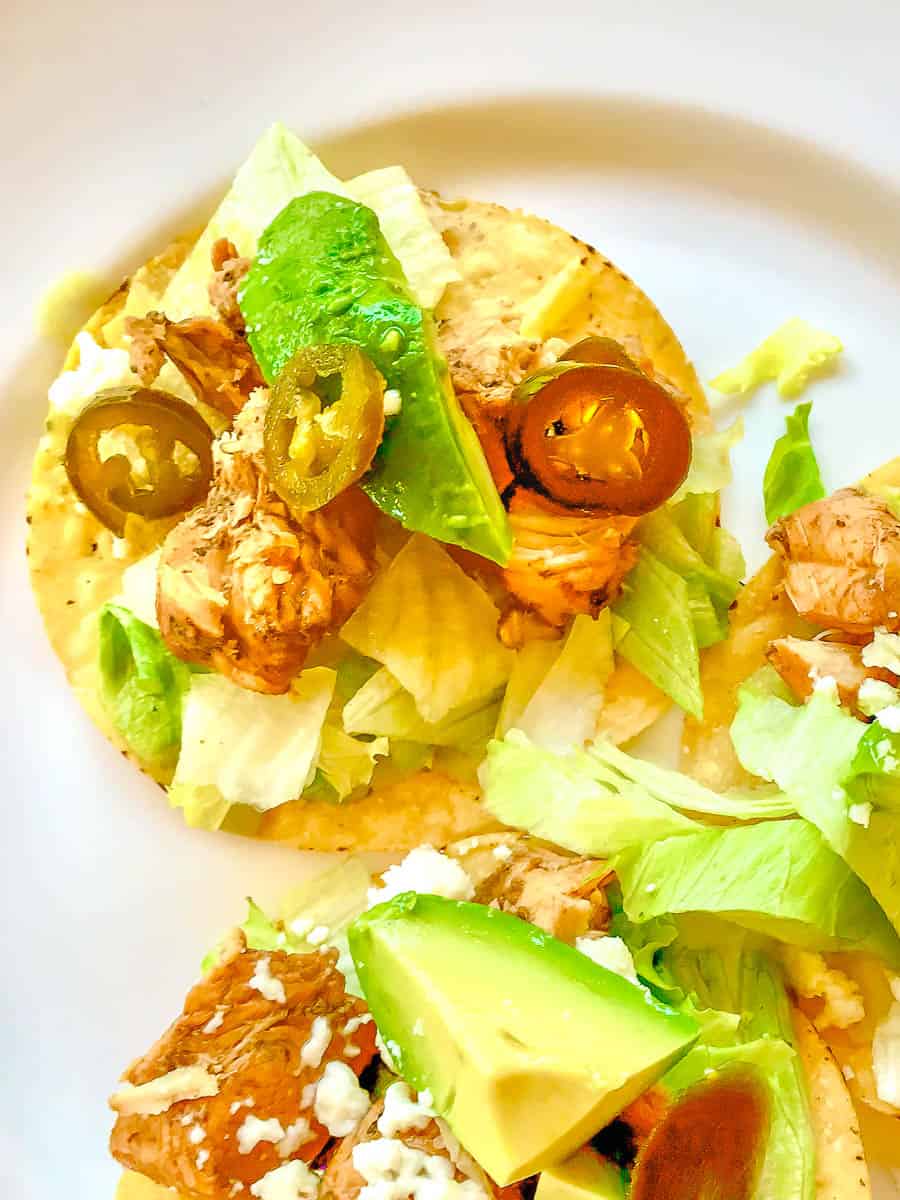 Three tostadas on white plate with lettuce, chicken and candied jalapenos