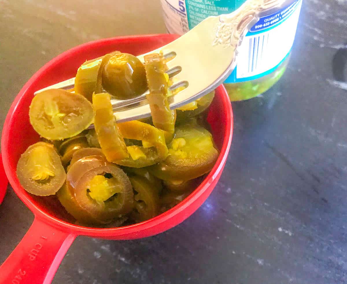 Jalapenos in a measuring cup with a fork