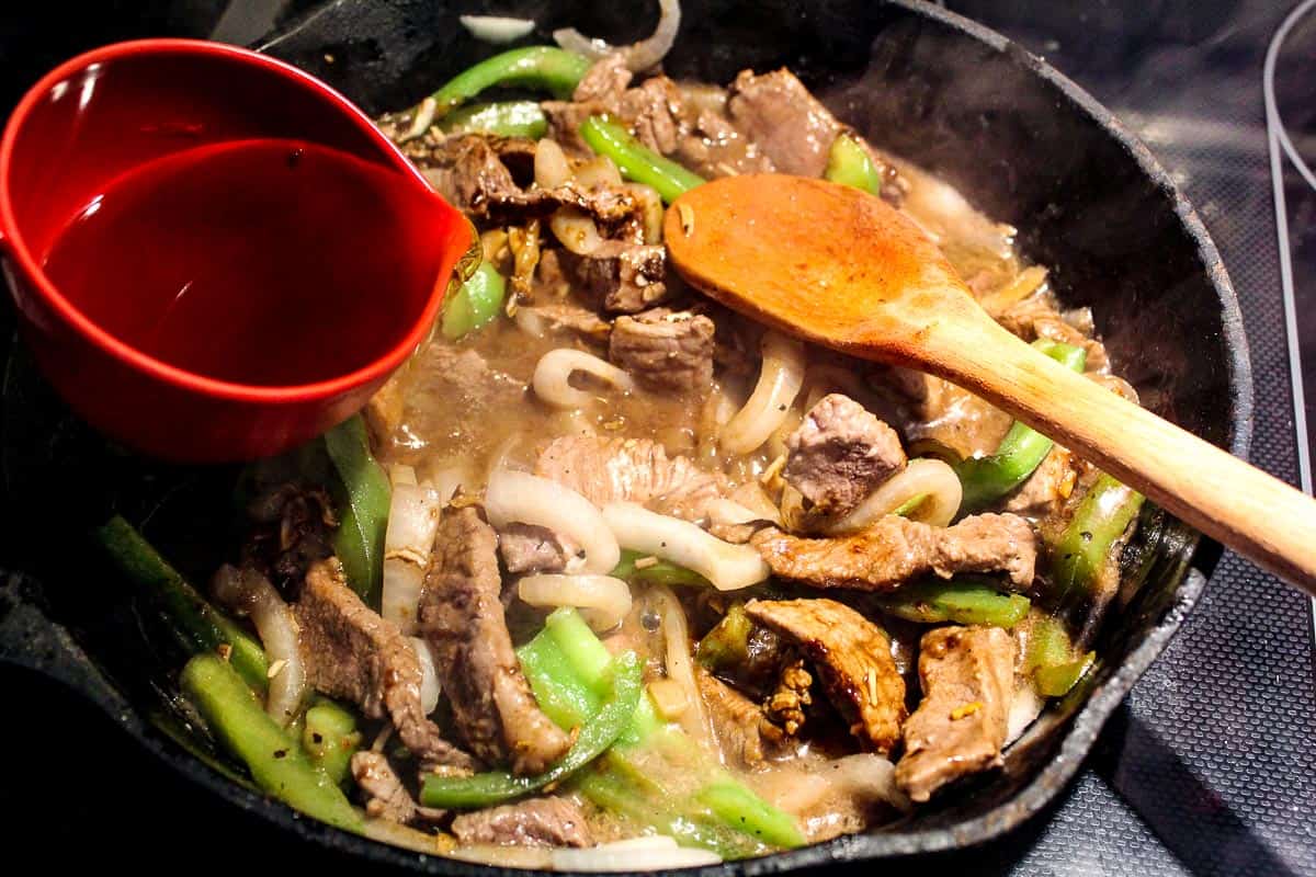 Sliced beef, onions and peppers and broth in pan.
