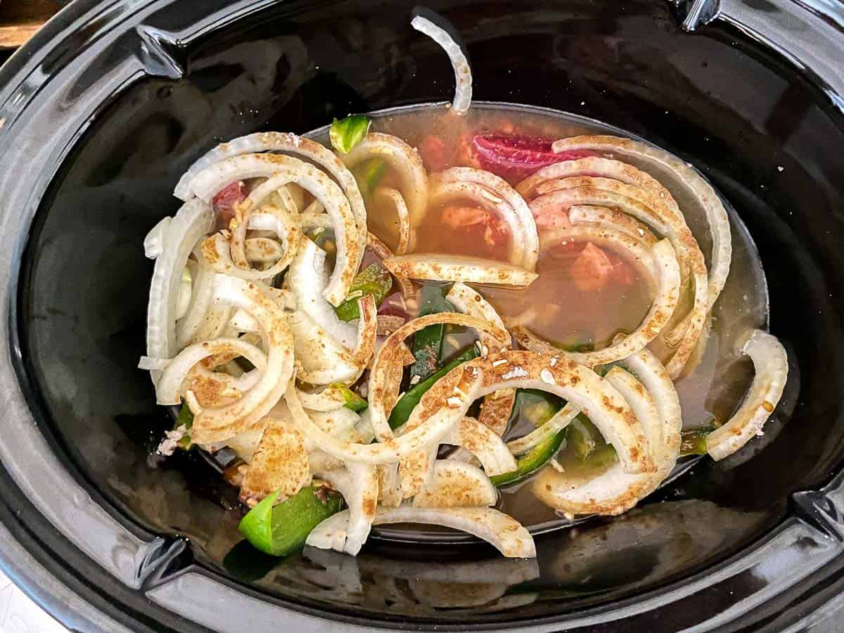 Sliced onions, peppers and beef in crockpot.