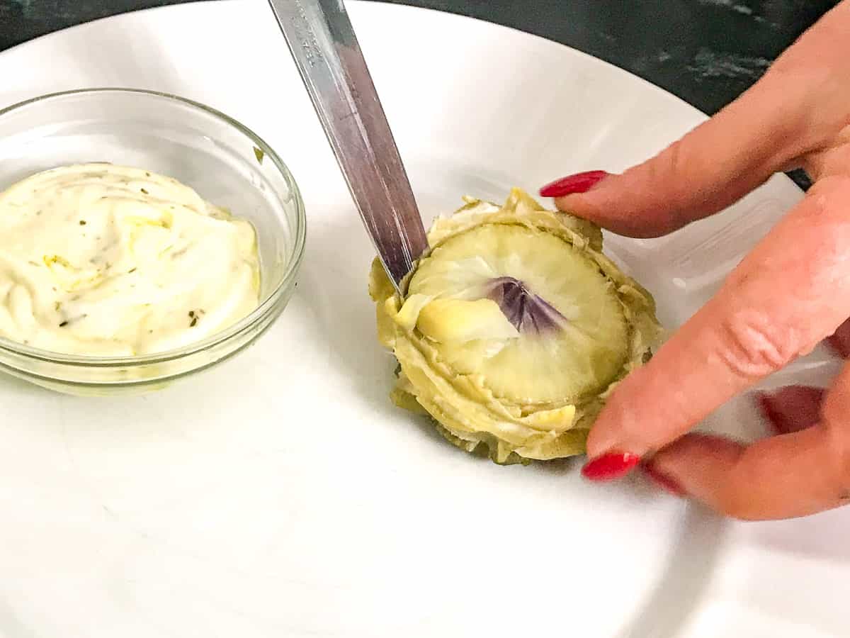 Knife being inserted into artichoke heart on white plate