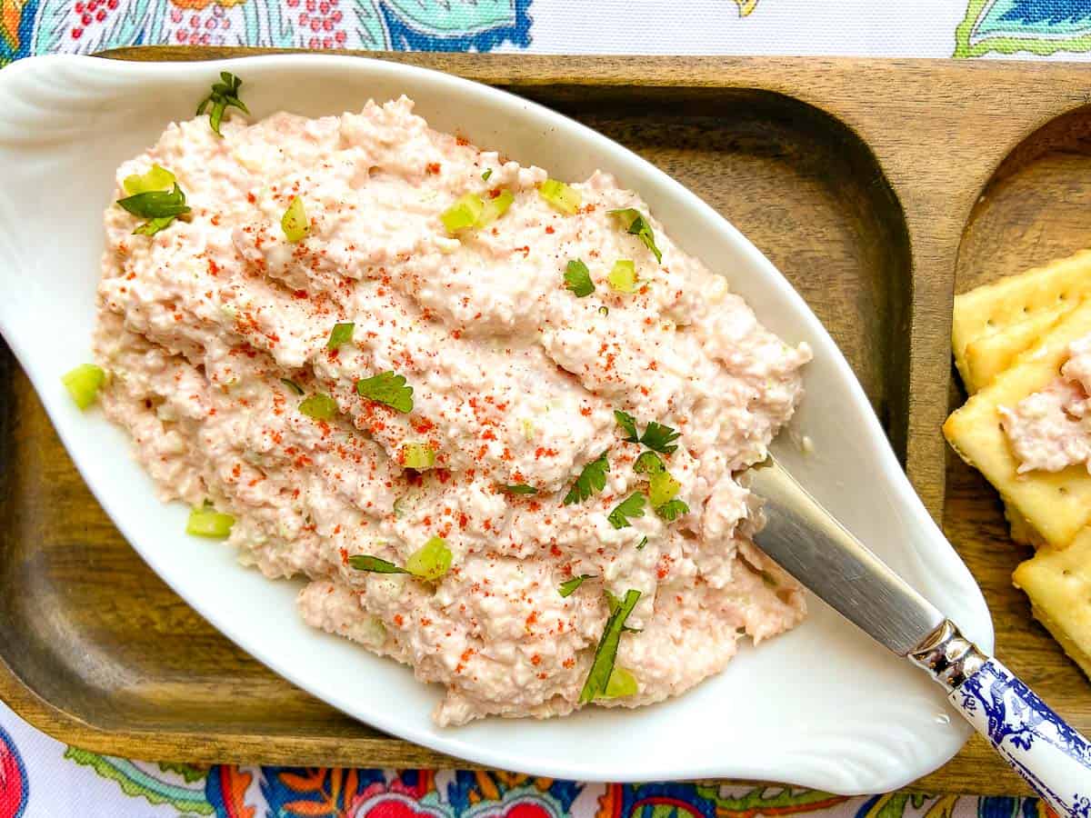 Deviled ham spread in a white oval bowl with a spreader and a side of crackers.