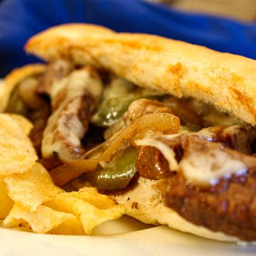 Philly cheesesteak sandwich on hoagie roll with a side of potato chips