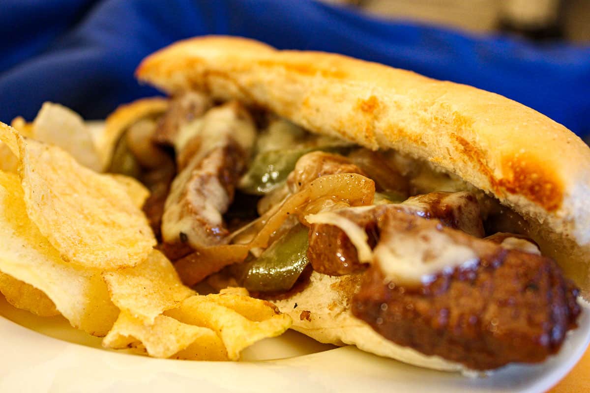 Philly cheesesteak sandwich on hoagie roll with a side of potato chips